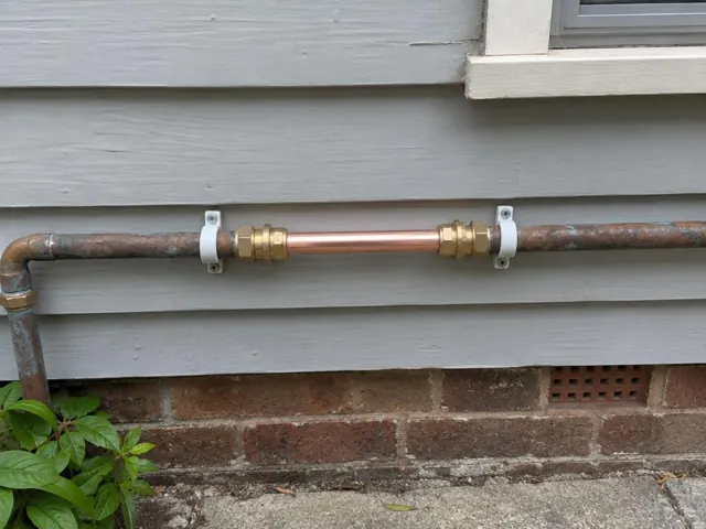 Repaired copper water pipe on exterior weatherboard wall above brick base in Northbridge