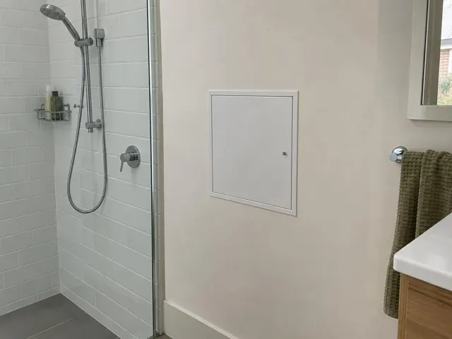 Small white access panel on a painted bathroom wall beside a shower and towel rail in Northbridge